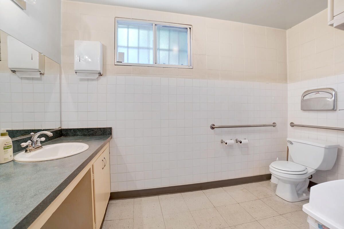 Public bathroom with white tile walls, sink, toilet, and a window.