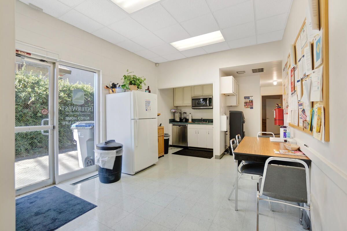 Kitchen with white refrigerator, stainless steel appliances, table, chairs, and bulletin board. Sliding glass door leads outside.