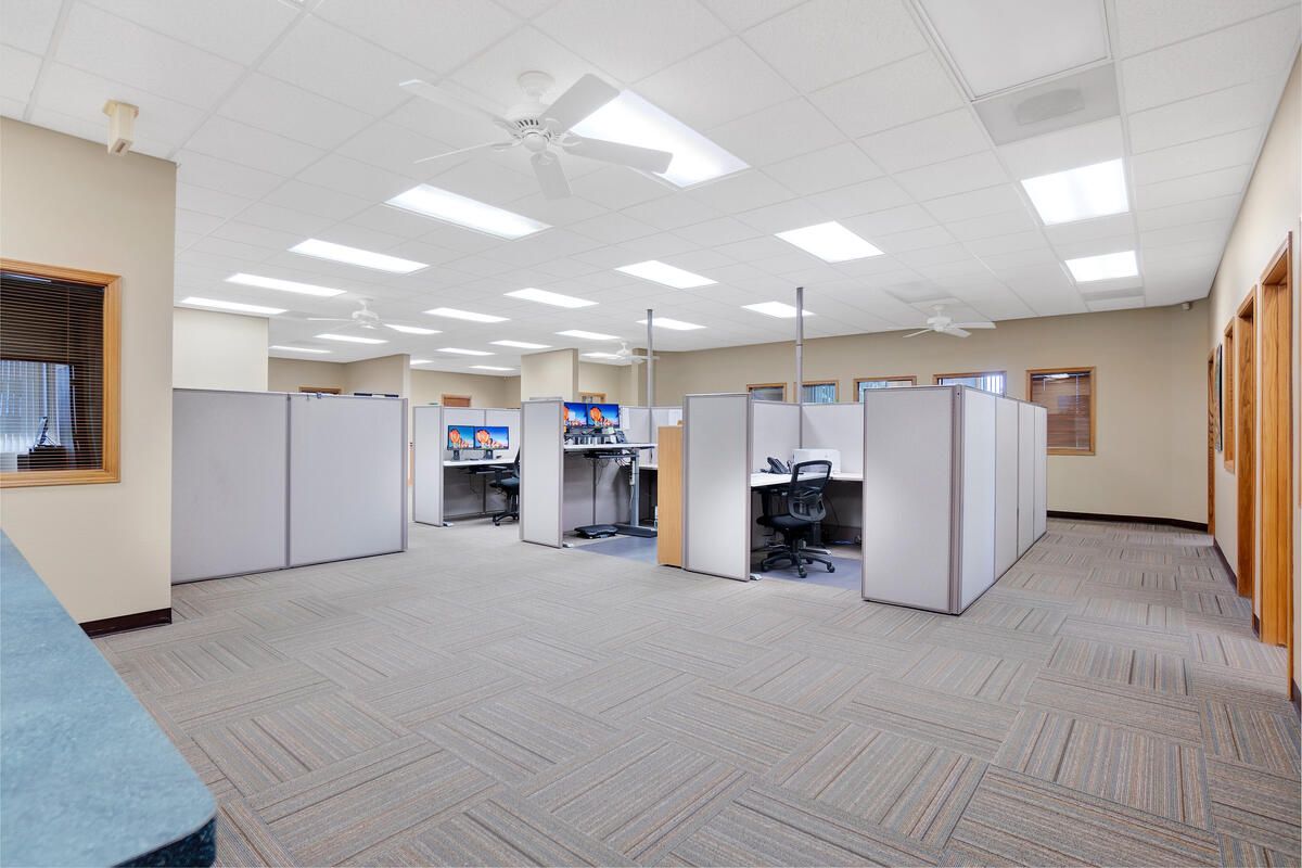 Office interior with cubicles, white ceiling lights, and patterned carpet.