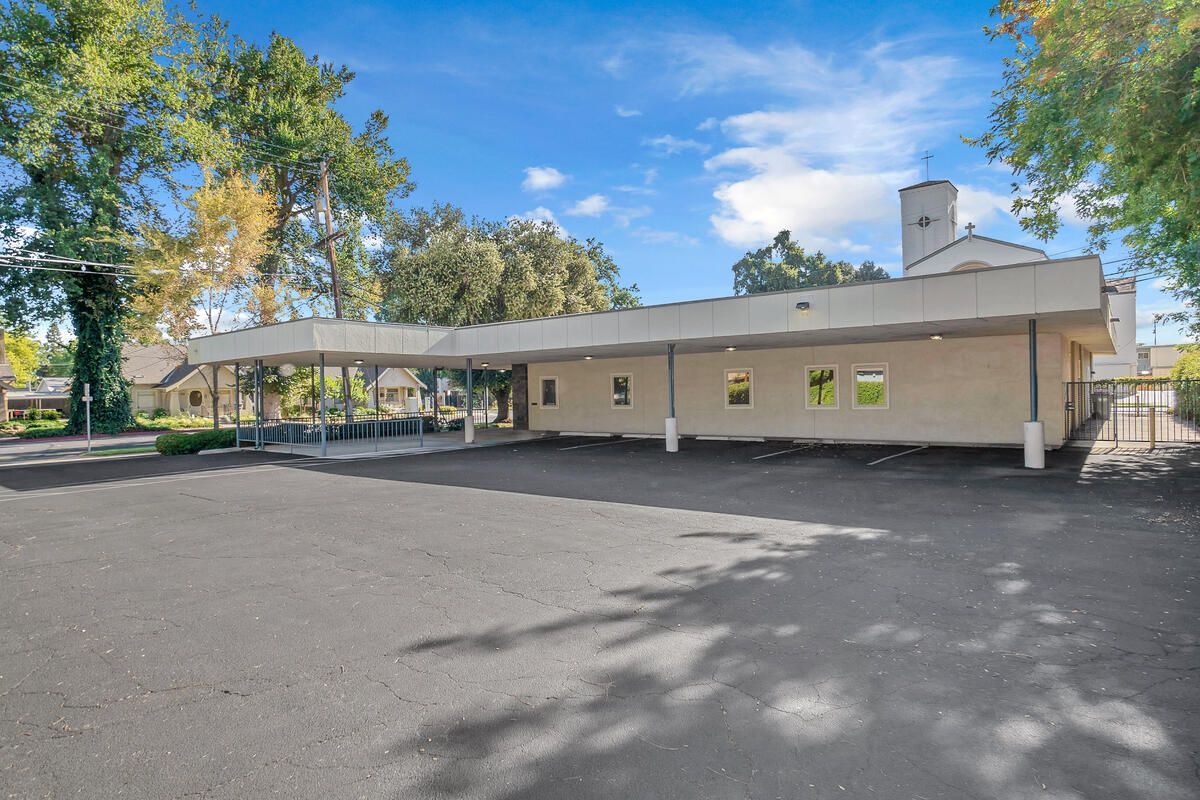 Exterior view of a single-story building with a covered walkway and asphalt parking lot under a blue sky.