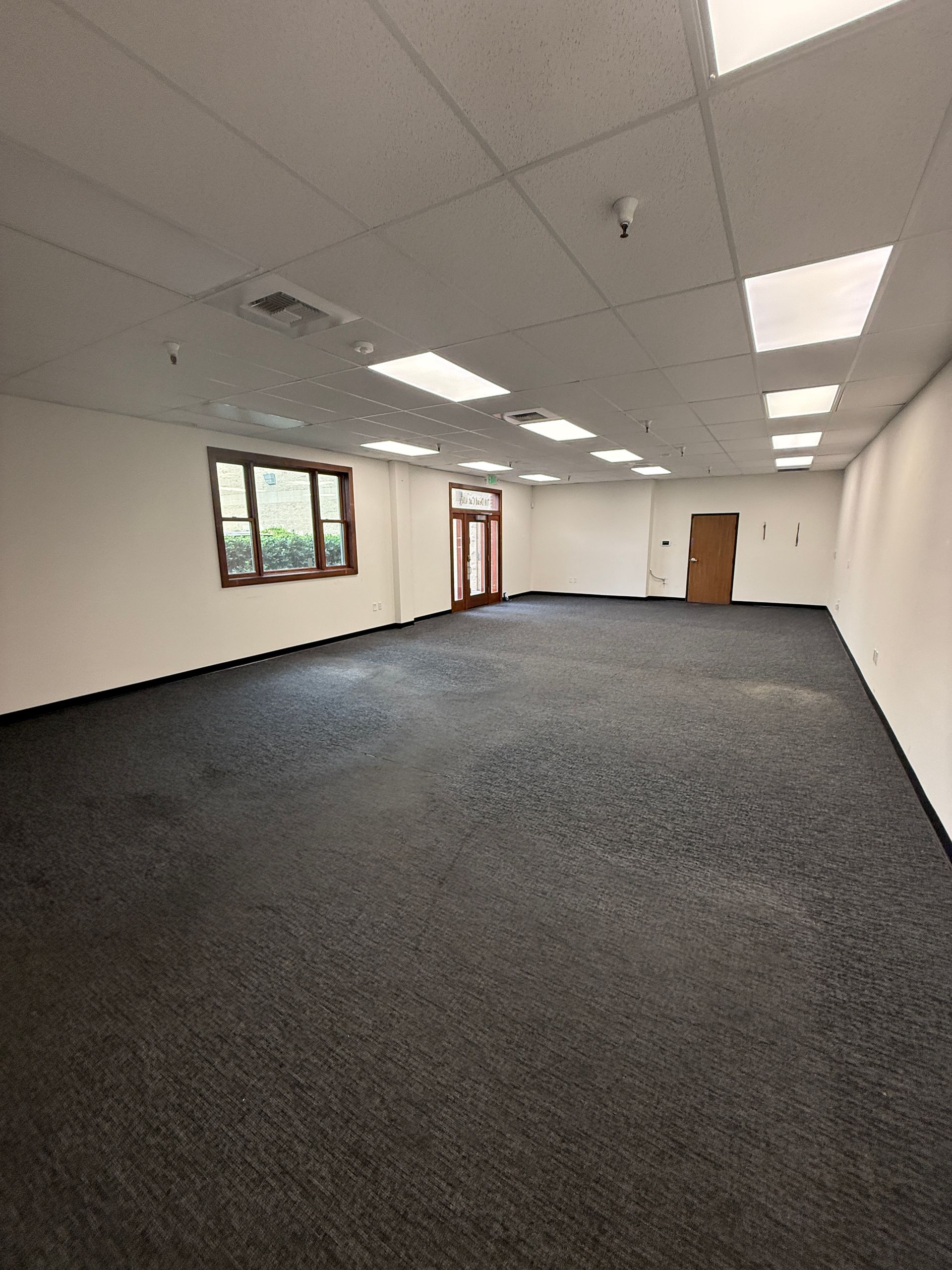 Empty office space with dark carpet, white walls and ceiling, and several ceiling lights.