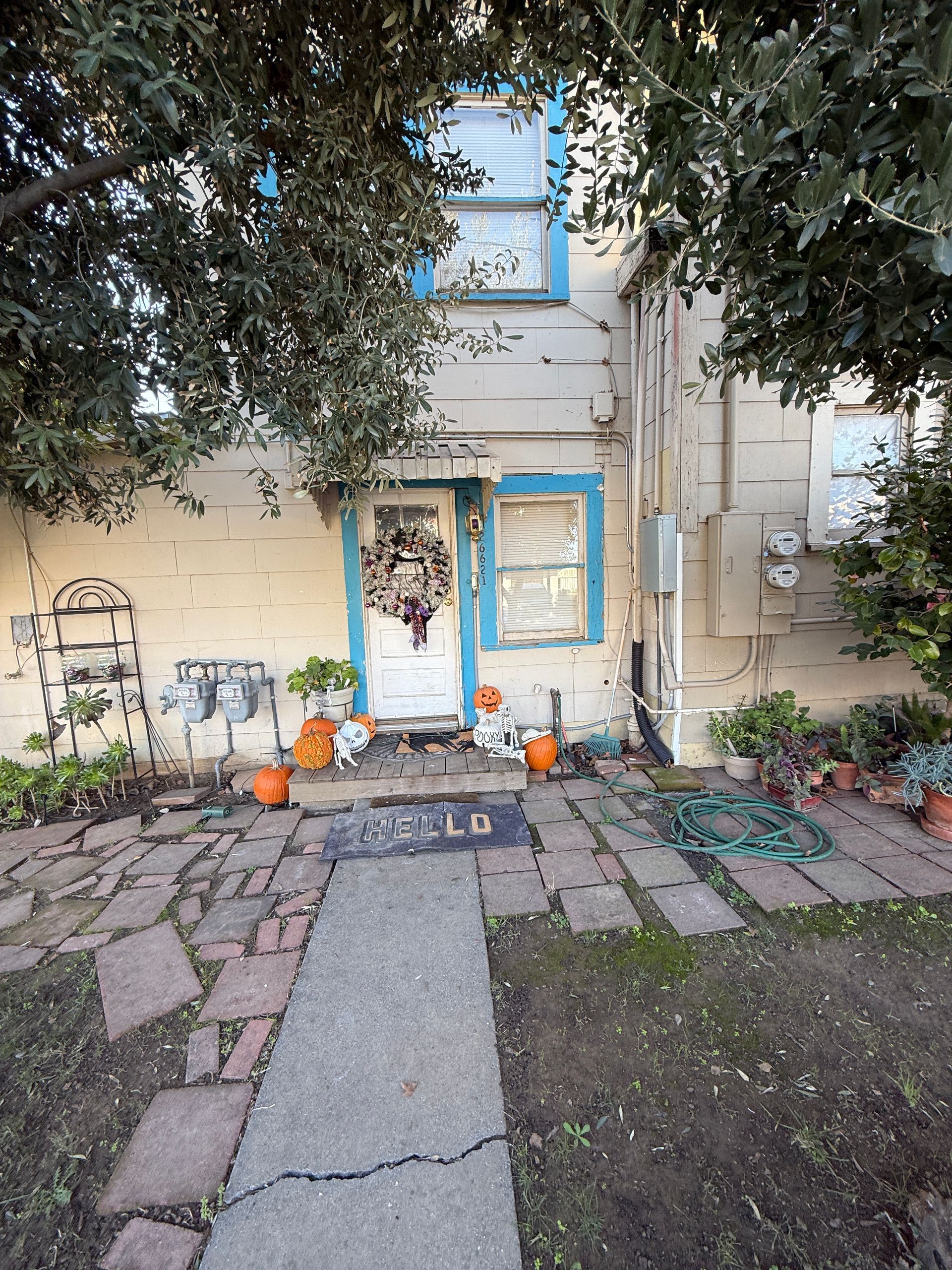 Two-story house with blue-trimmed windows. Door decorated with a wreath. Pumpkins and welcome mat. Brick walkway.