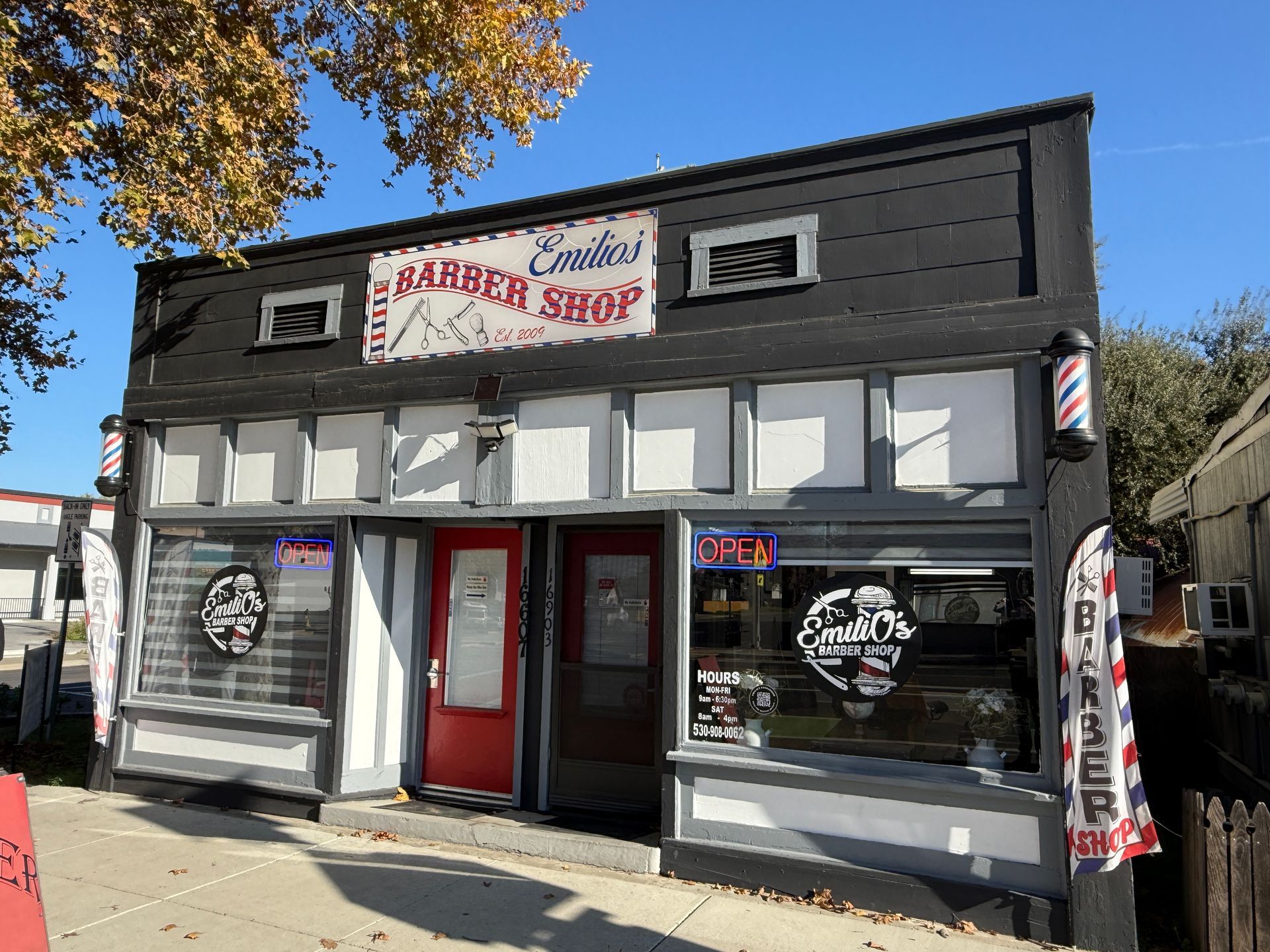 Exterior of Eskins Barber Shop: Black building, red door, barber poles, shop sign.