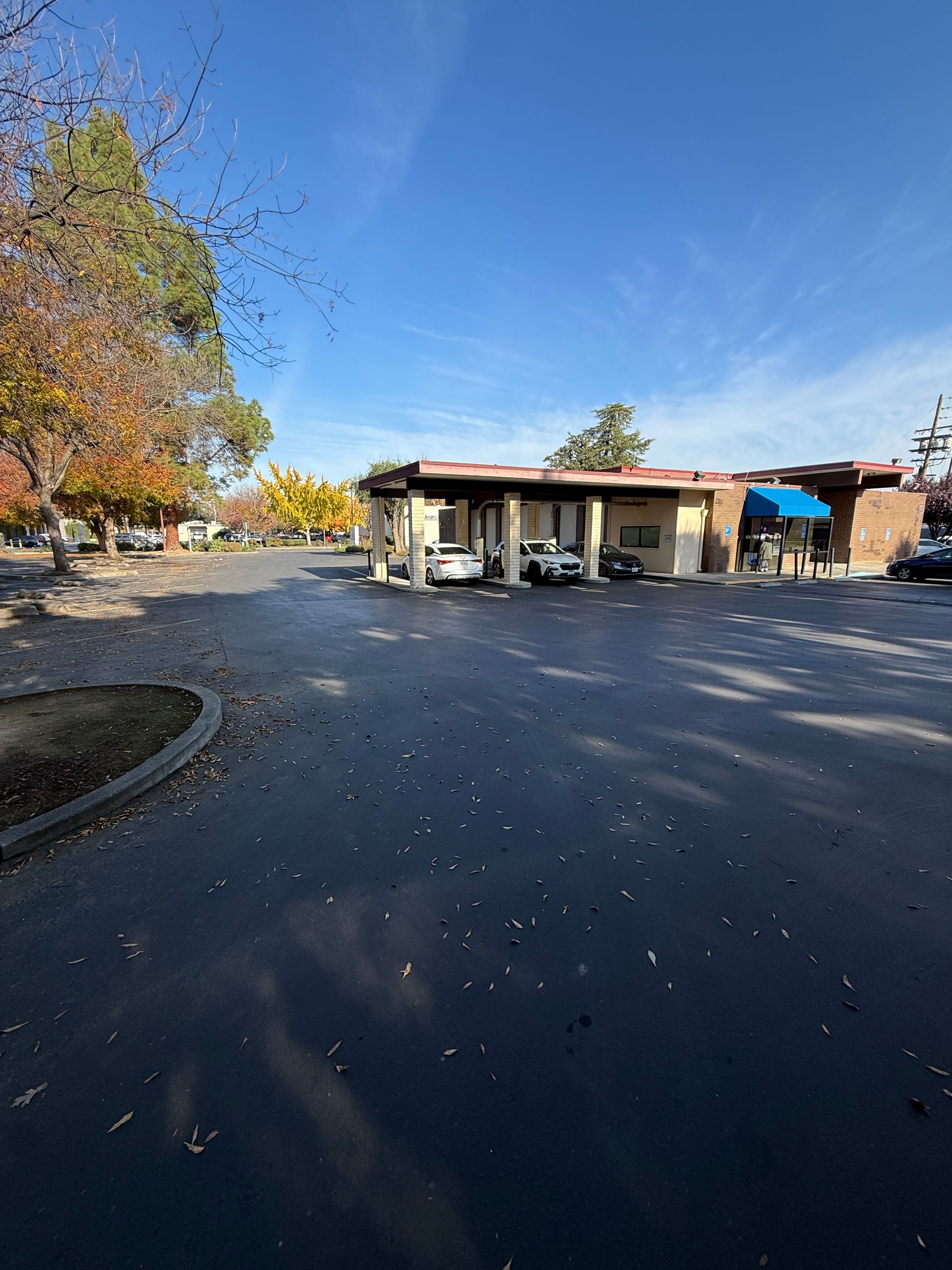 Exterior shot of a small, single-story building under a blue sky, with cars parked out front, and some trees with fall foliage.