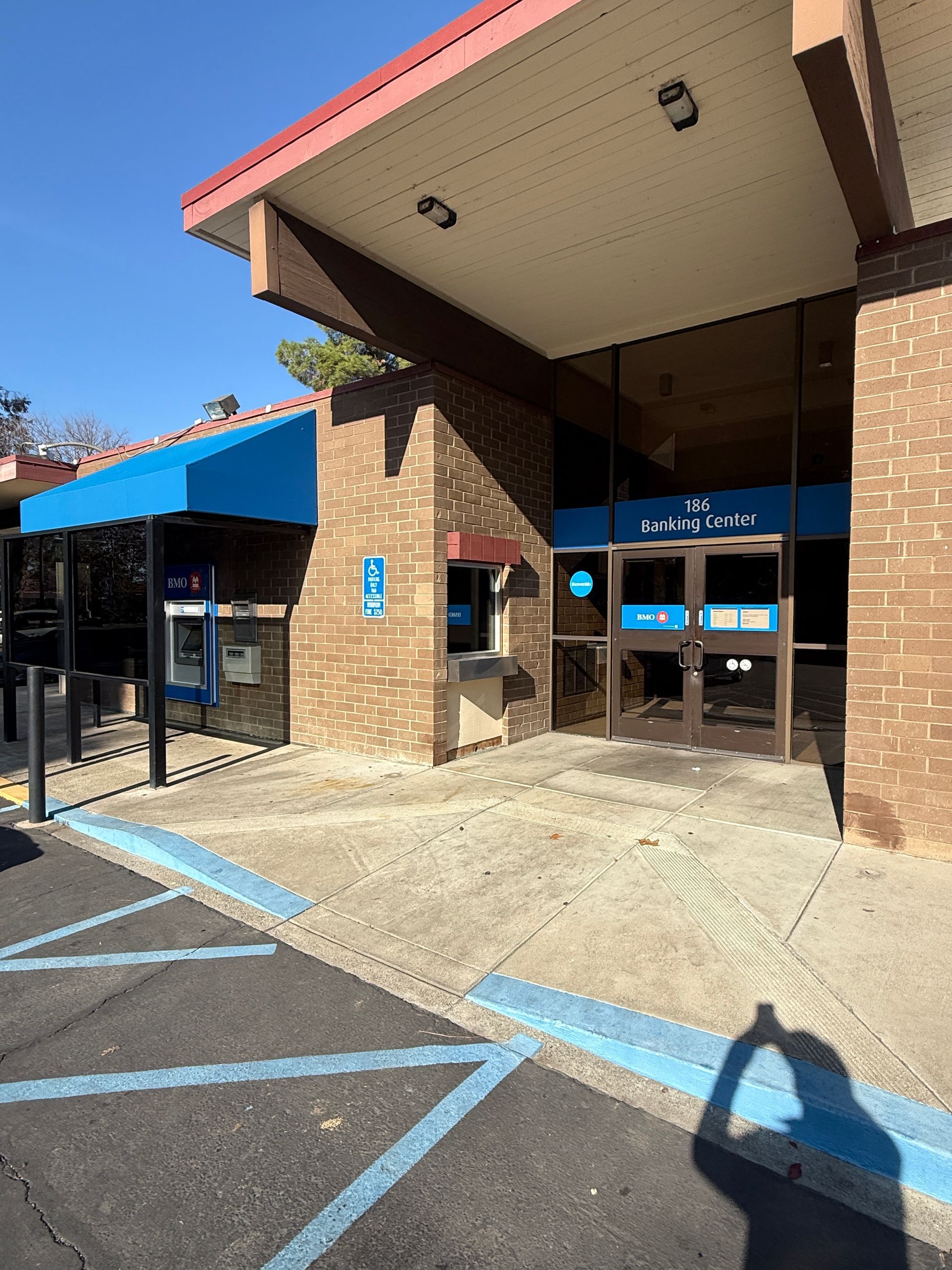Exterior view of a brick building with a blue awning and glass doors. ATM on left, entrance on right, blue handicap spot.
