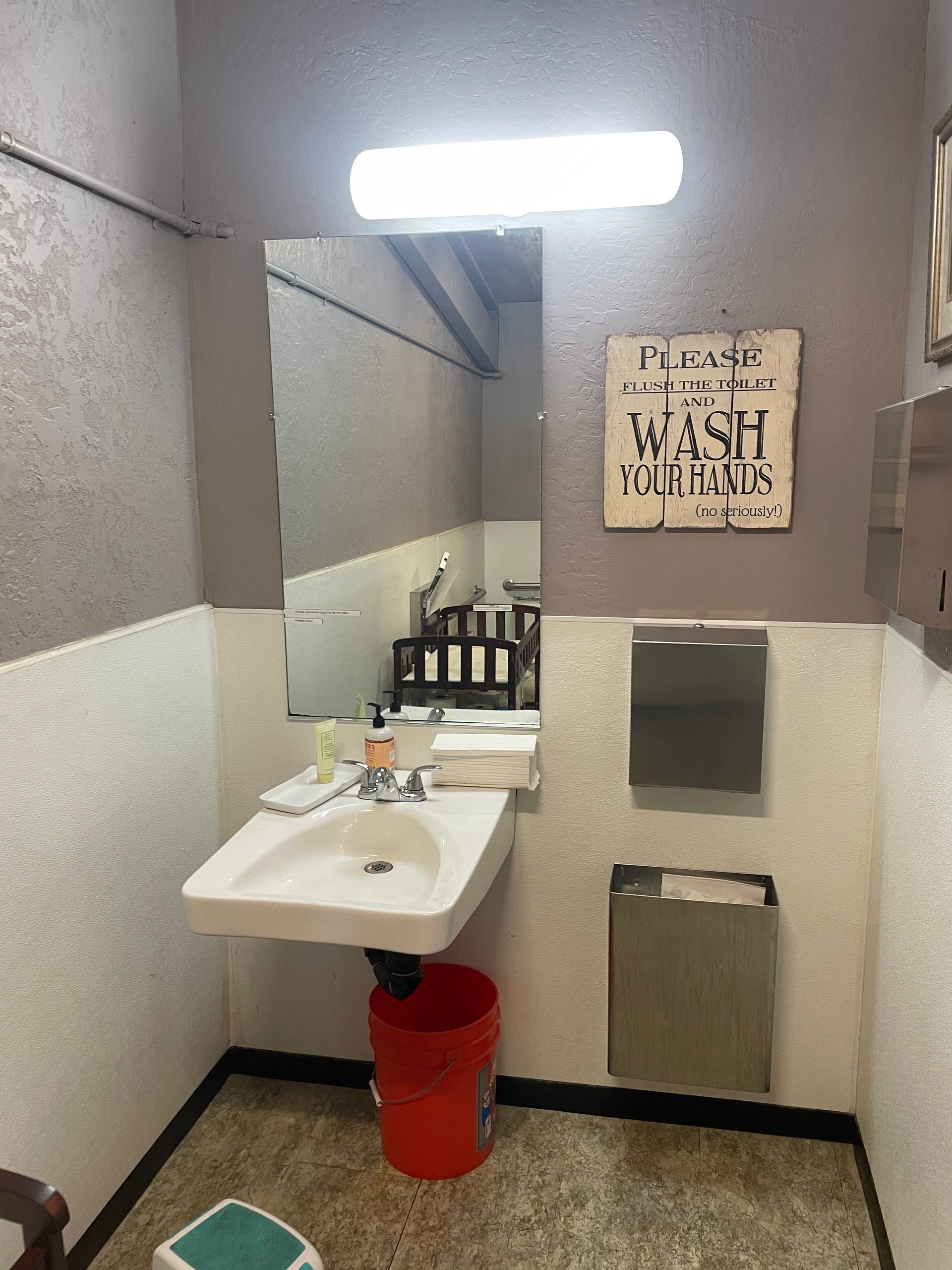 A bathroom with a sink and a sign that says please wash your hands