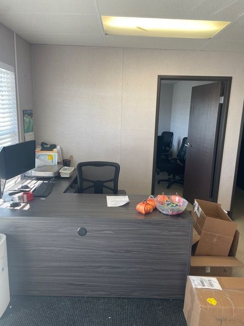 An office with a desk, chair, and open doorway to another room with chairs.