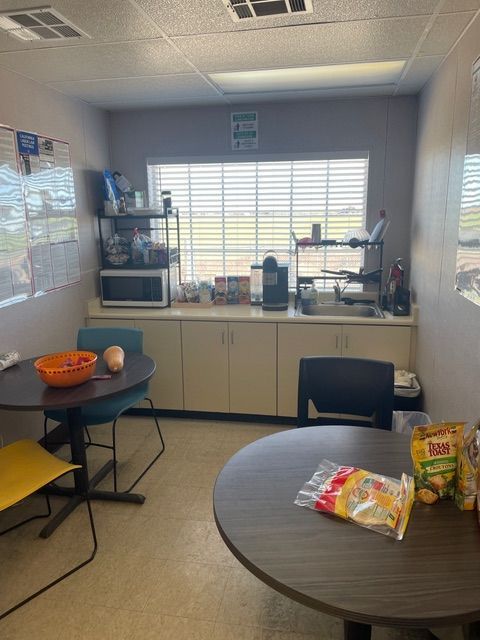 Office break room with tables, cabinets, microwave, and sink near a window.