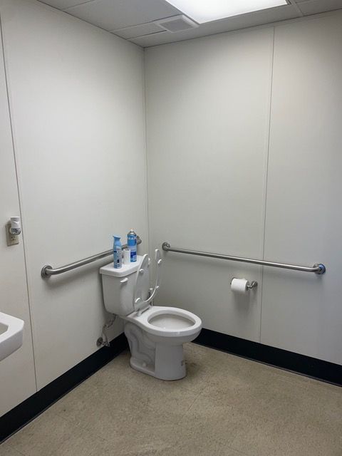 ADA accessible restroom with a toilet, grab bars, and a roll of toilet paper on a white and light-colored floor.
