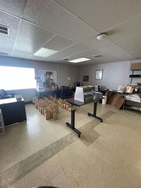 A bright office with beige floor, brown paper bags, a table, and office supplies.
