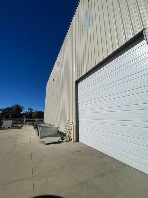 White warehouse with a closed overhead door, against a bright blue sky. Concrete paved area.