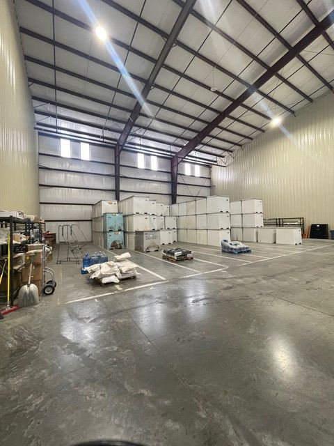 Inside of a warehouse, mostly empty, with pallets of stacked white boxes and supplies, gray floor.