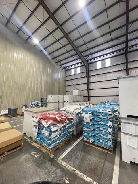 Warehouse interior with pallets stacked with blue and red bags, metal walls and ceiling.