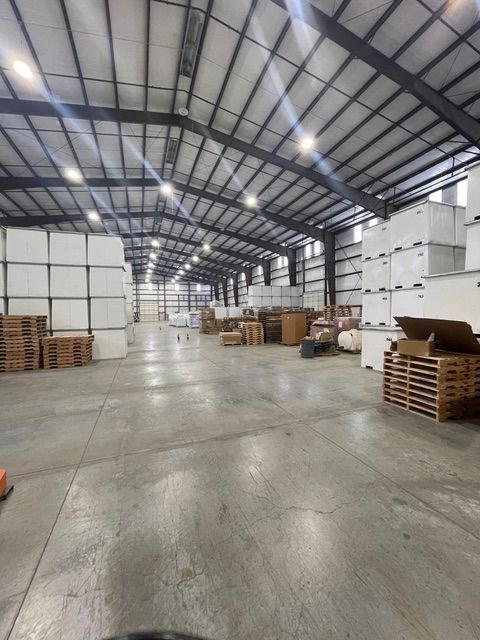 Inside of a large warehouse; stacks of white boxes and pallets of wood are visible.
