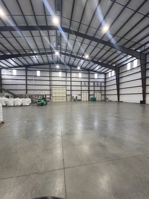 Spacious warehouse interior with a polished concrete floor, forklift, and storage bags. Steel beams support the roof.