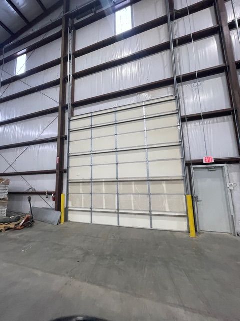 Large warehouse interior with a closed overhead door and an exit door on the right.