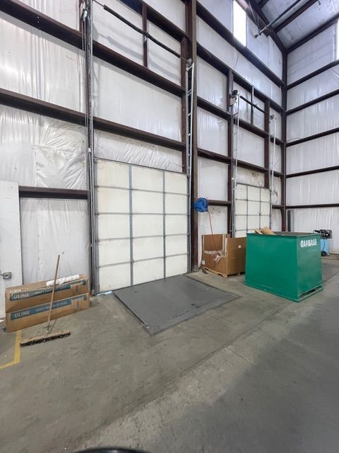 Interior warehouse view with closed white overhead doors, boxes, and a metal platform on the floor.