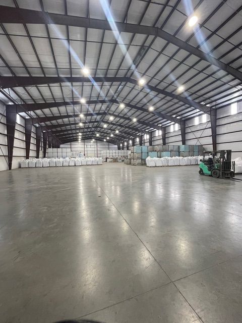 Large warehouse interior filled with stacks of white bags. A forklift is on the right.