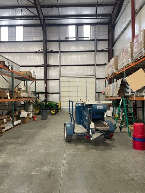 Interior of a warehouse with shelving, machinery, and a closed garage door. A John Deere tractor is visible.