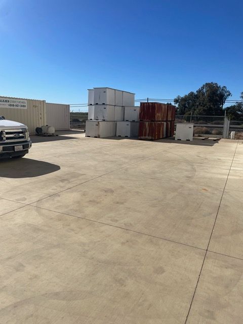 A concrete lot with stacked storage containers under a blue sky, a truck is parked on the left.