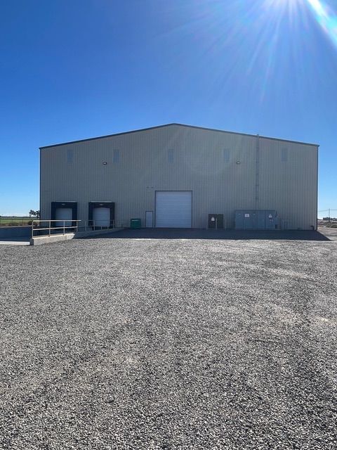 Warehouse building with loading docks on a gravel lot under a bright, sunny sky.