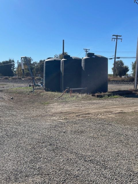 Three dark water tanks in a gravel lot near railroad tracks under a clear blue sky.