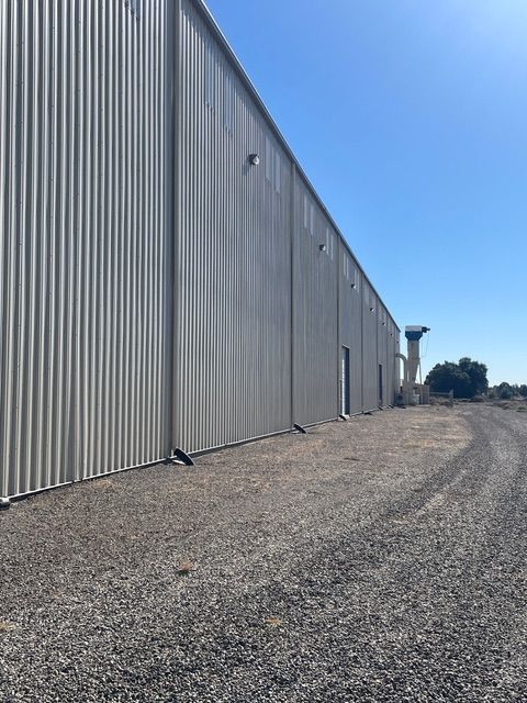 Exterior view of a long, corrugated metal industrial building against a clear blue sky.
