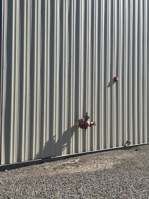 Tan corrugated metal wall with red fire hydrants and gravel ground.