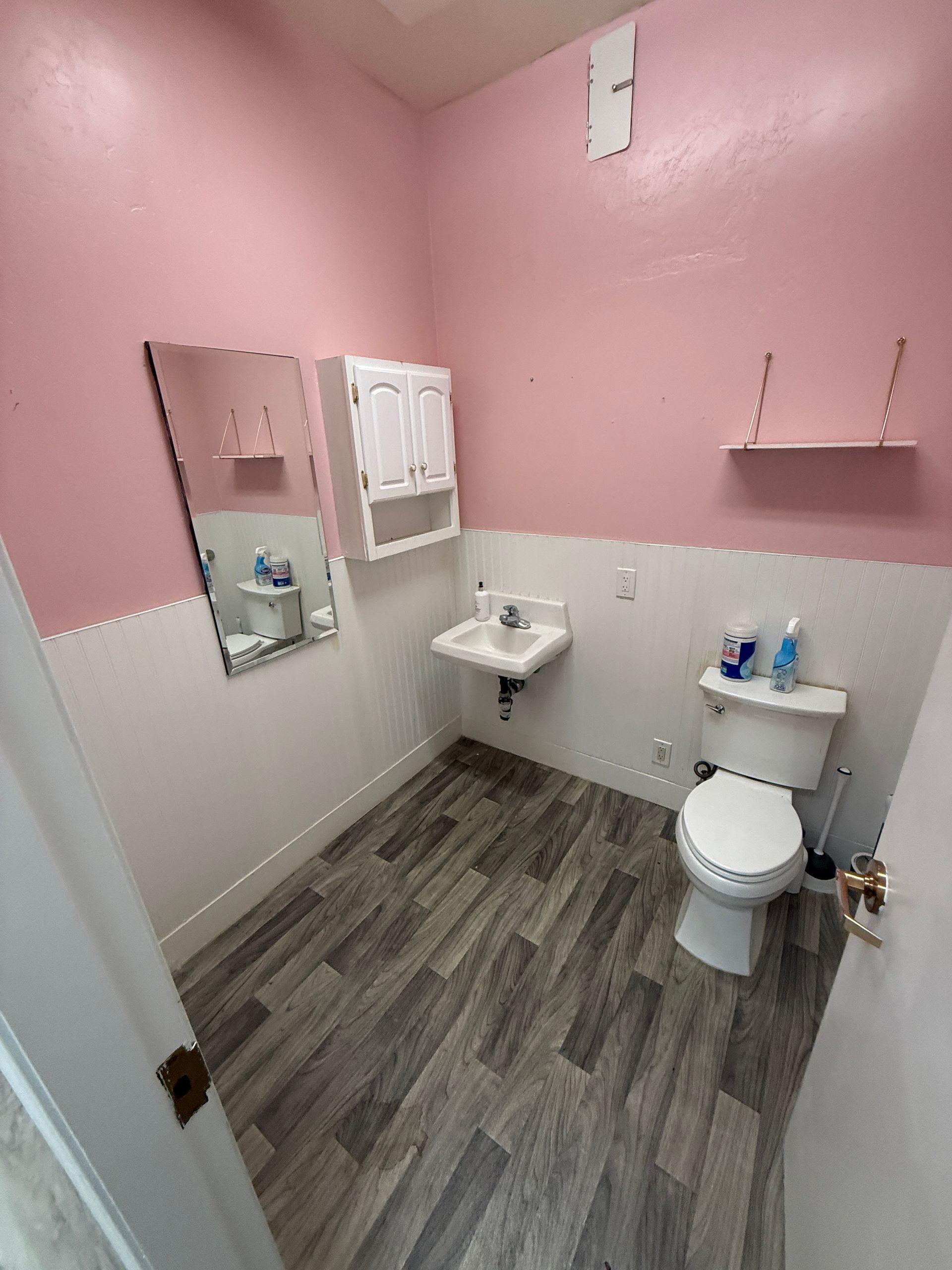 A bathroom with pink walls , a toilet , sink and mirror.