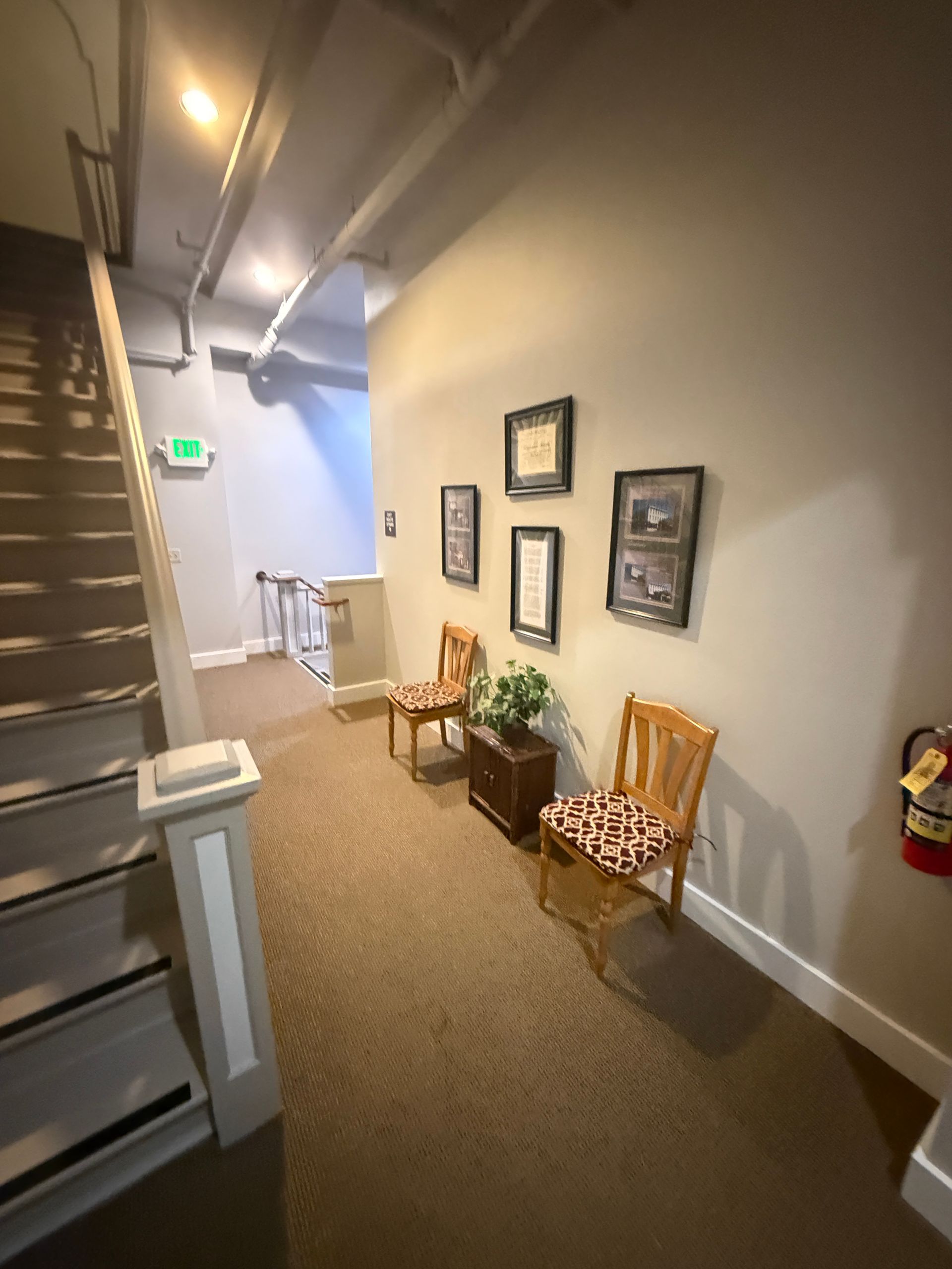 A hallway with stairs and chairs and a fire extinguisher