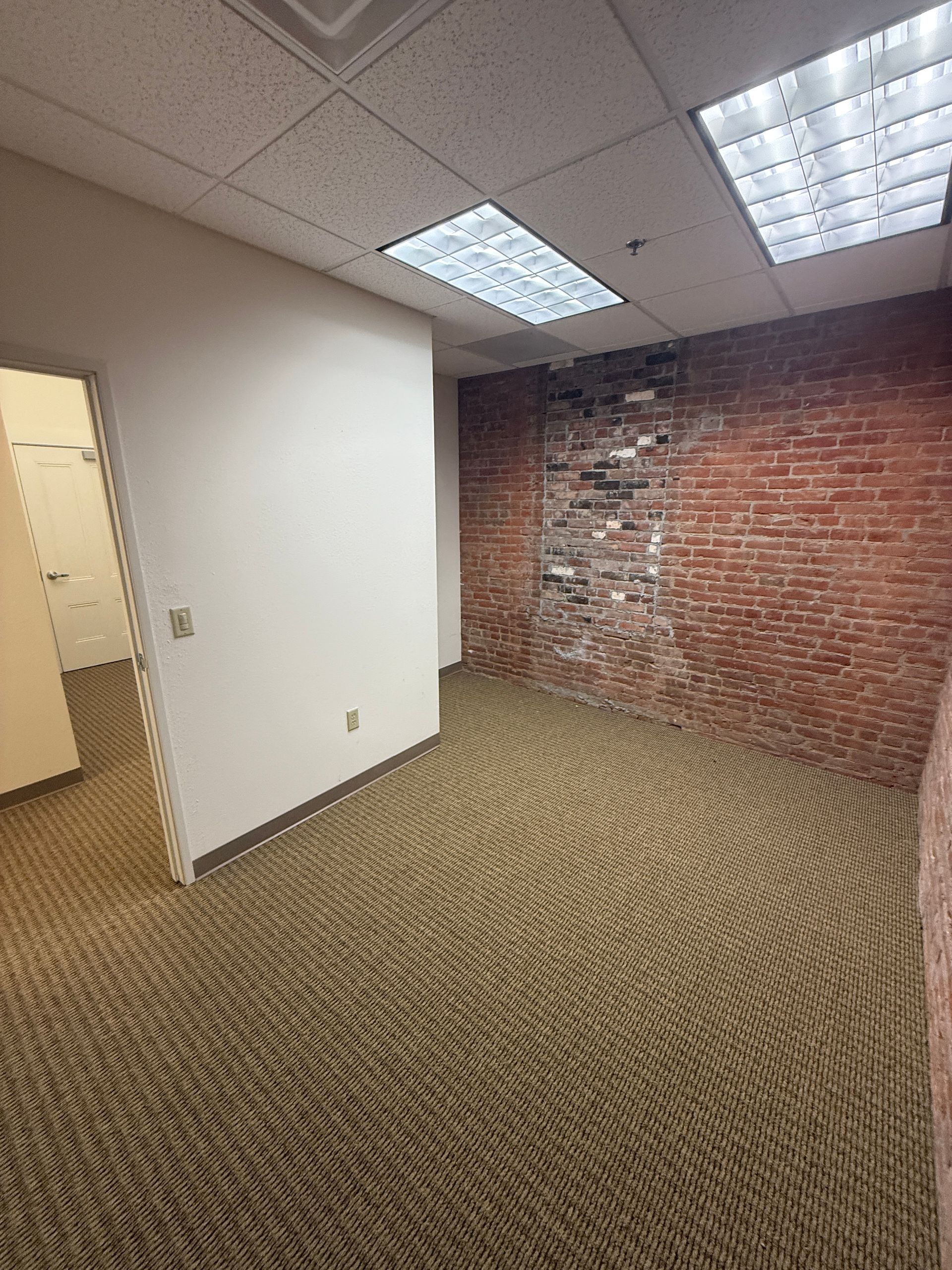 An empty room with a brick wall and a carpeted floor.