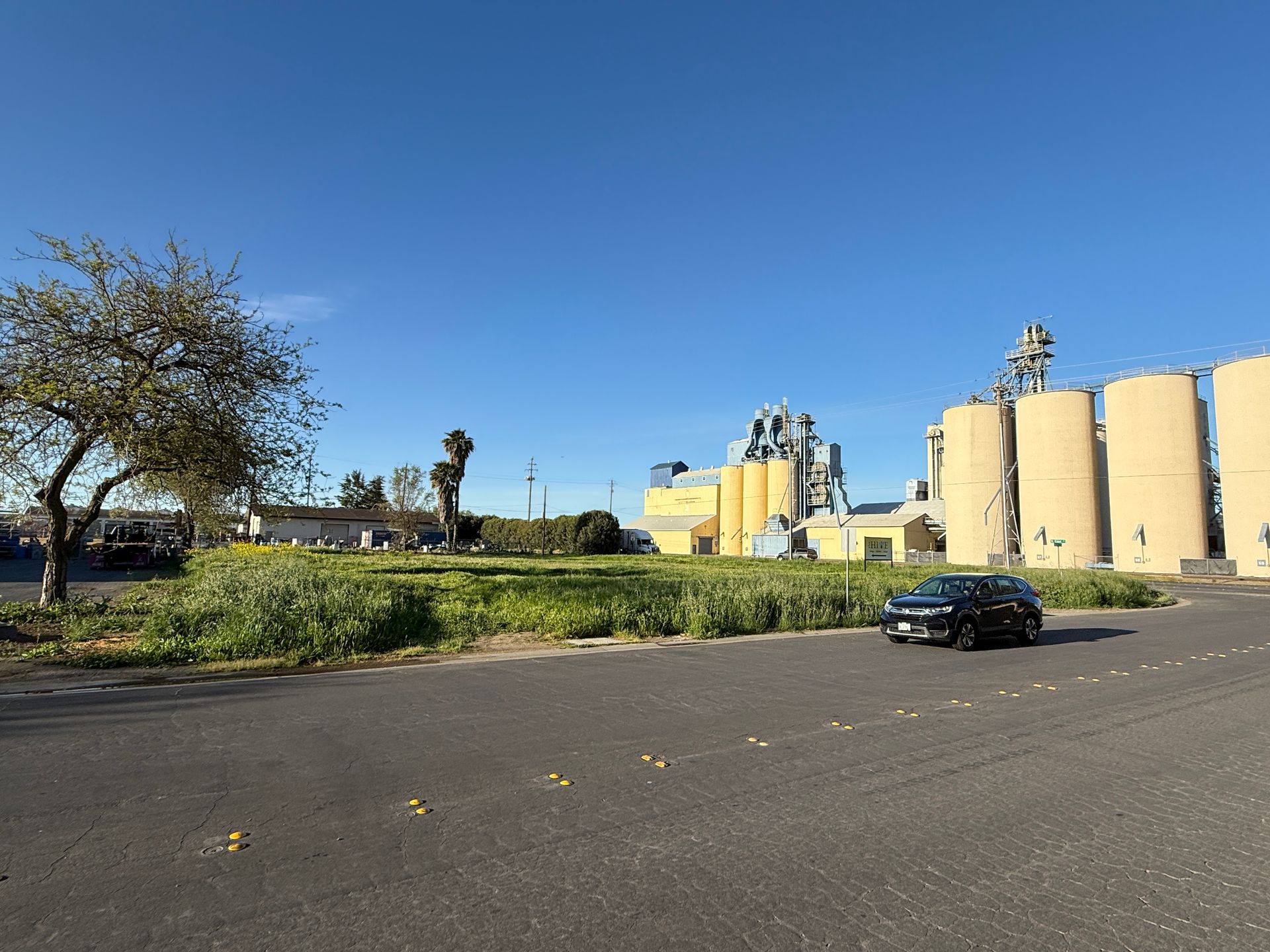 A car is parked on the side of the road in front of a factory.