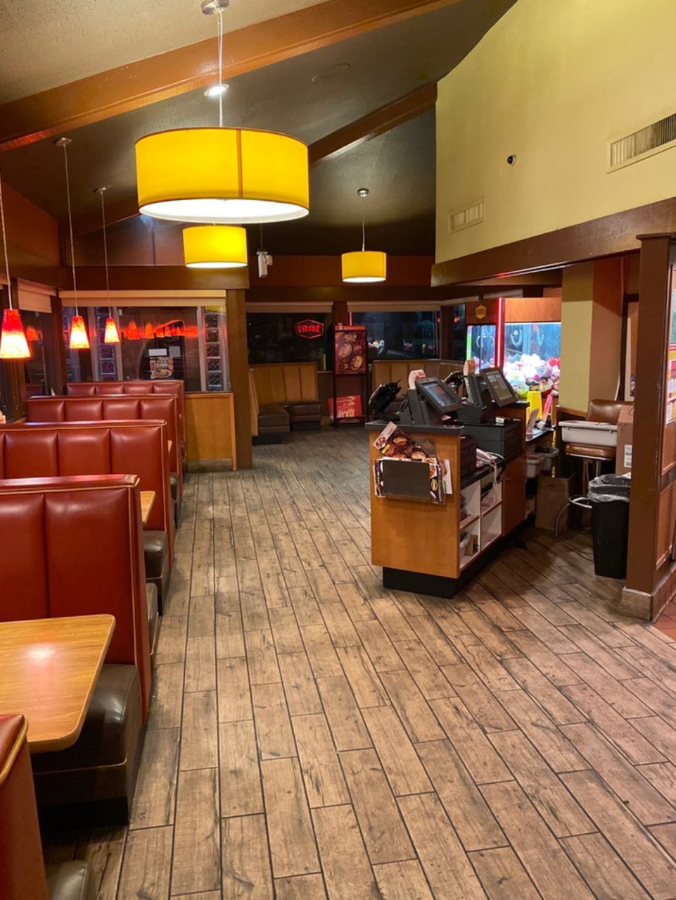 Interior of a restaurant with booths, wooden floors, and hanging yellow lamps. Empty dining area.