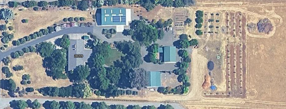Aerial view of buildings, trees, and fields. Includes roads and a solar panel array.