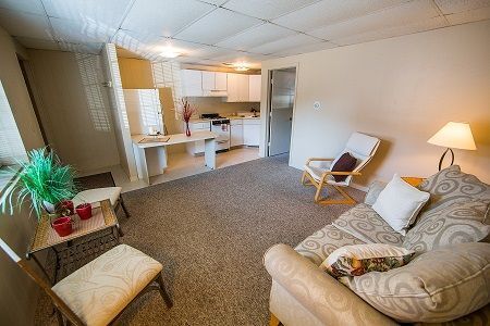 Photo showing a living room in the foreground with a kitchen in the background