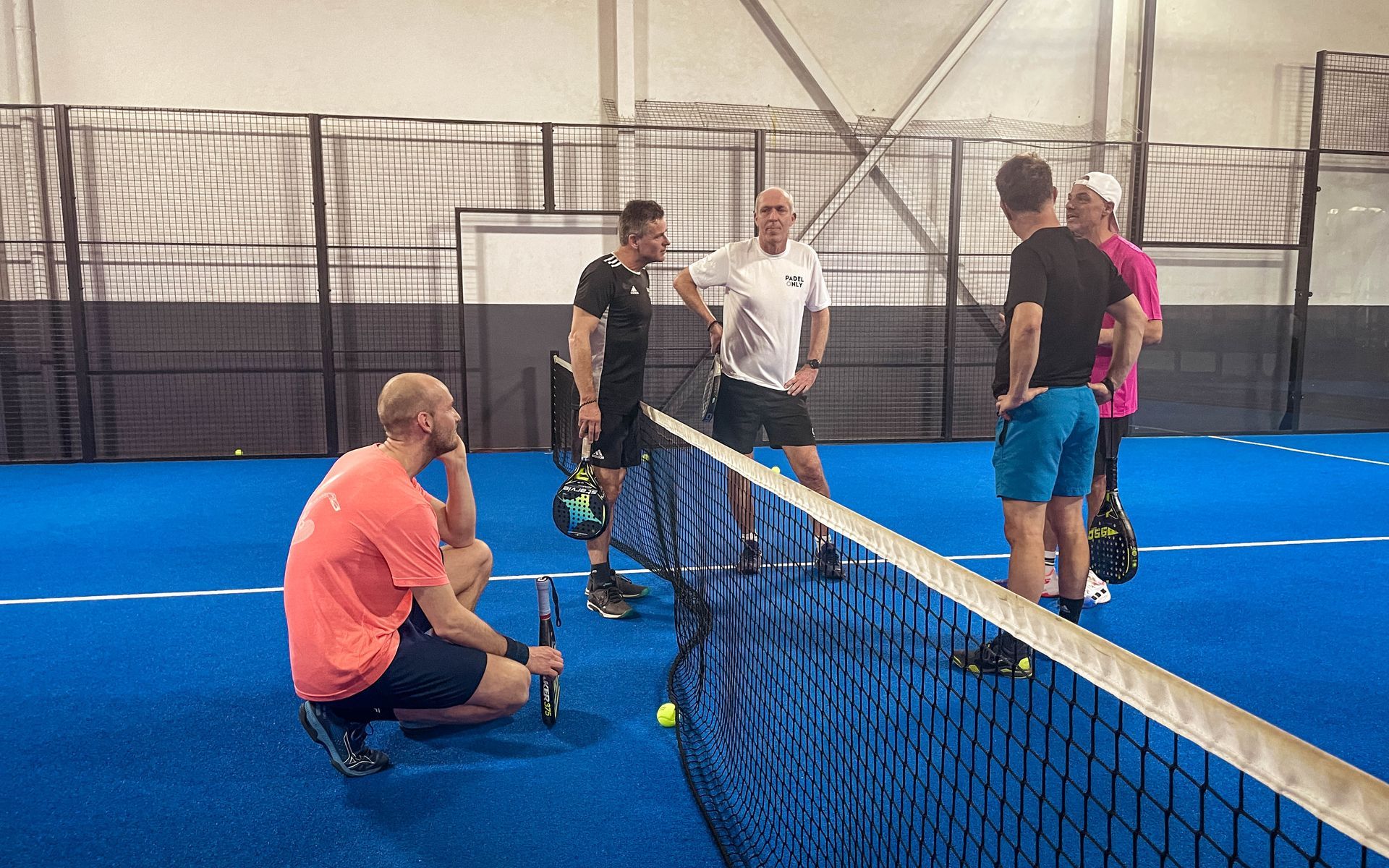 Een groep mannen staat rond een padelnet op een padelbaan.