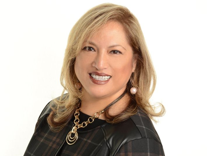 A woman wearing a plaid jacket and a necklace is smiling for the camera.