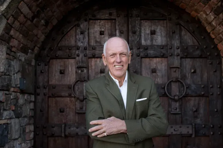 A man in a suit is standing in front of a wooden door.