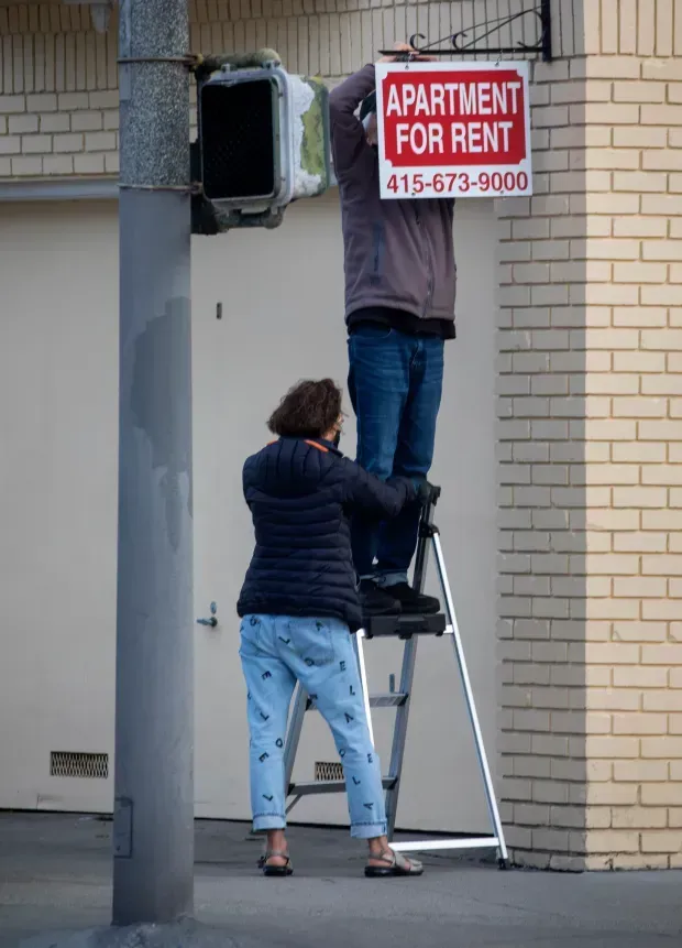 A man on a ladder hangs an apartment for rent sign
