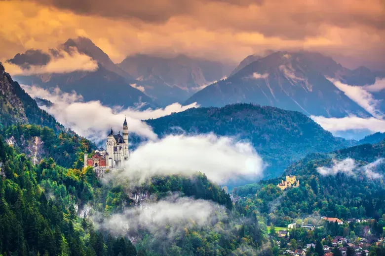 A castle sitting on top of a mountain surrounded by mountains and clouds.