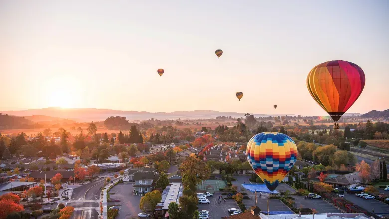 A group of hot air balloons are flying over a city at sunset.