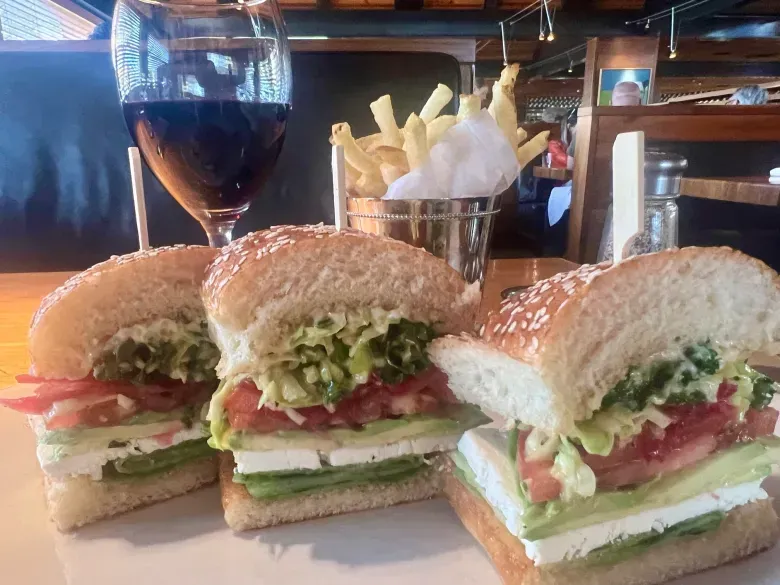 Three sandwiches are sitting on a white plate next to a glass of wine.