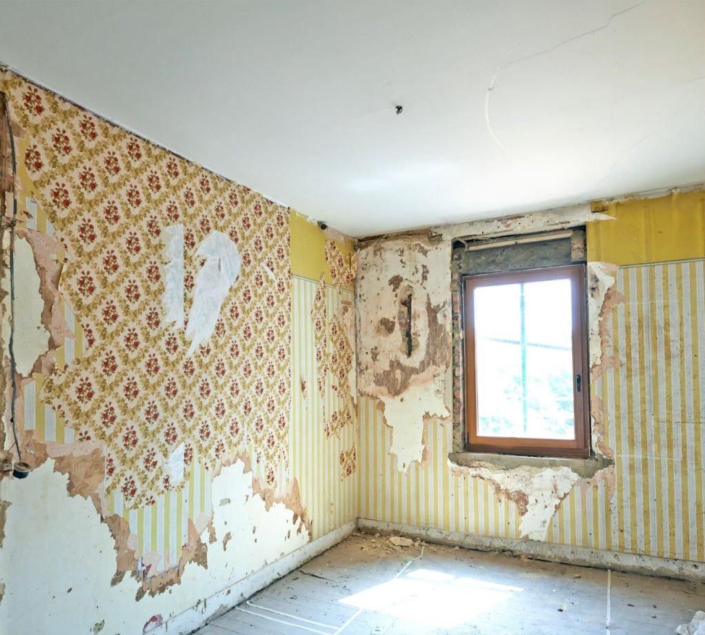 An empty room with peeling wallpaper and a window.