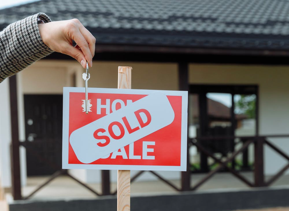 A person is holding a sold sign in front of a house.