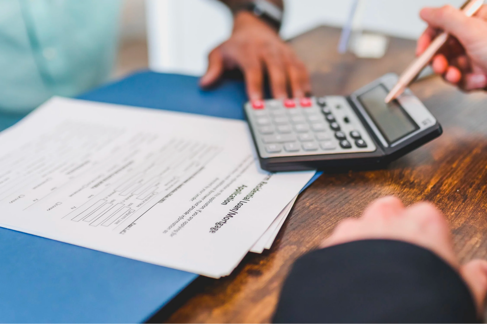 A person is using a calculator while another person is writing on a piece of paper.