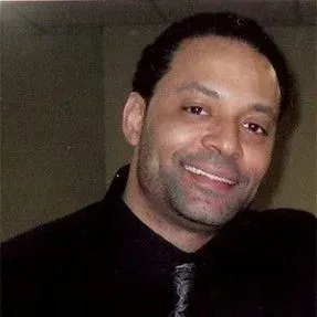 A man in a black shirt and tie is smiling for the camera.
