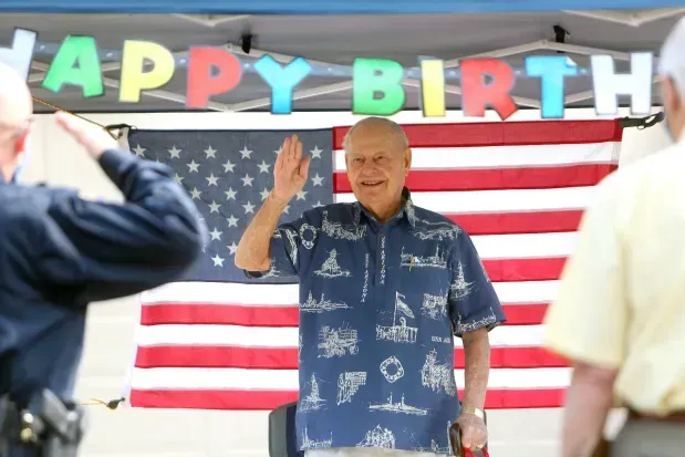 A man stands in front of an american flag under a happy birthday banner