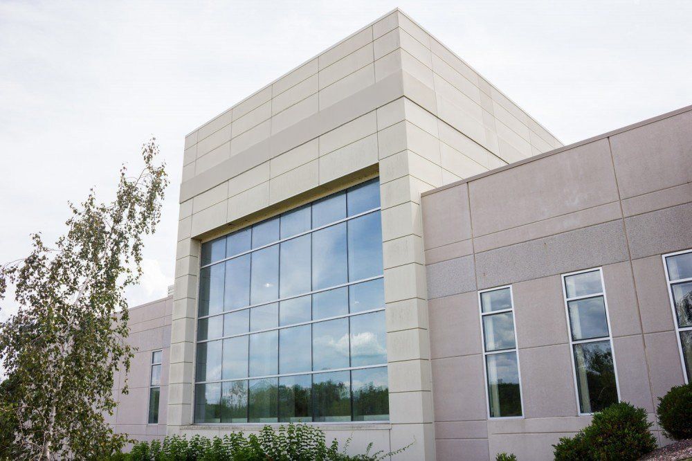 Modern tan building with large glass windows and cloudy sky reflection.
