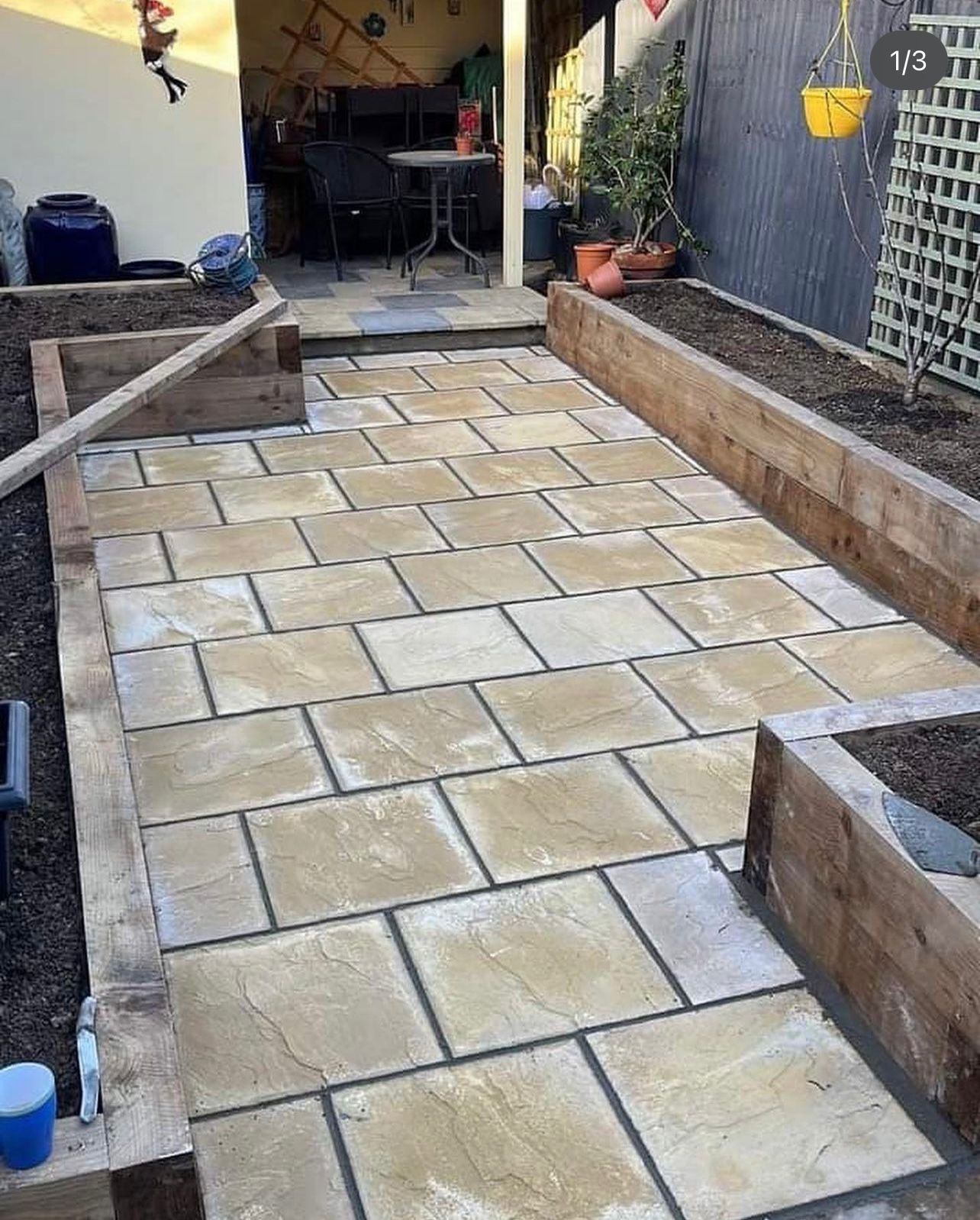 A patio with bricks and wooden planters in a backyard.