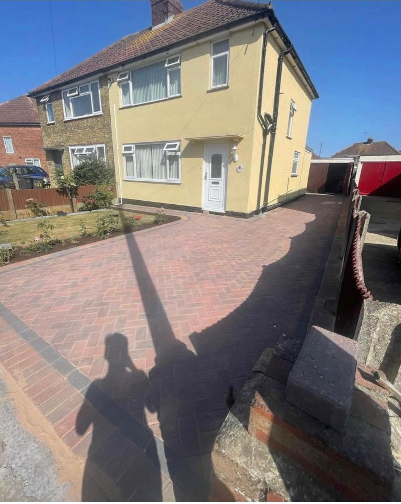 A shadow of a person is cast on a brick driveway in front of a house.